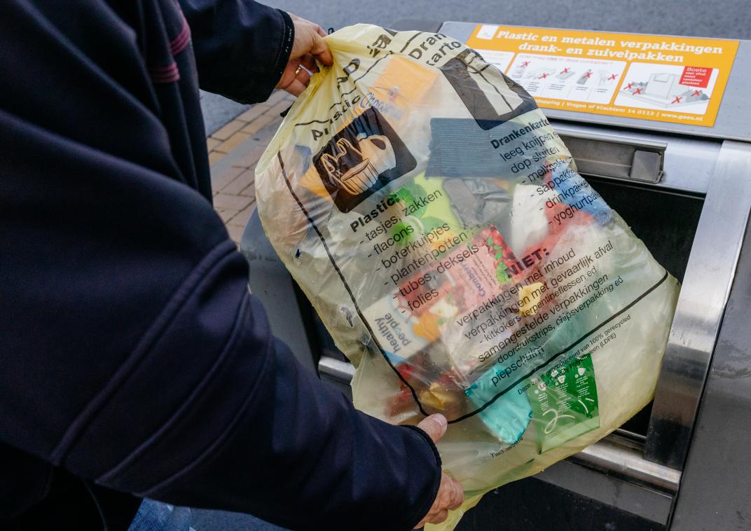 PMD afval in een doorzichtige zak wordt naar de PMD container gebracht